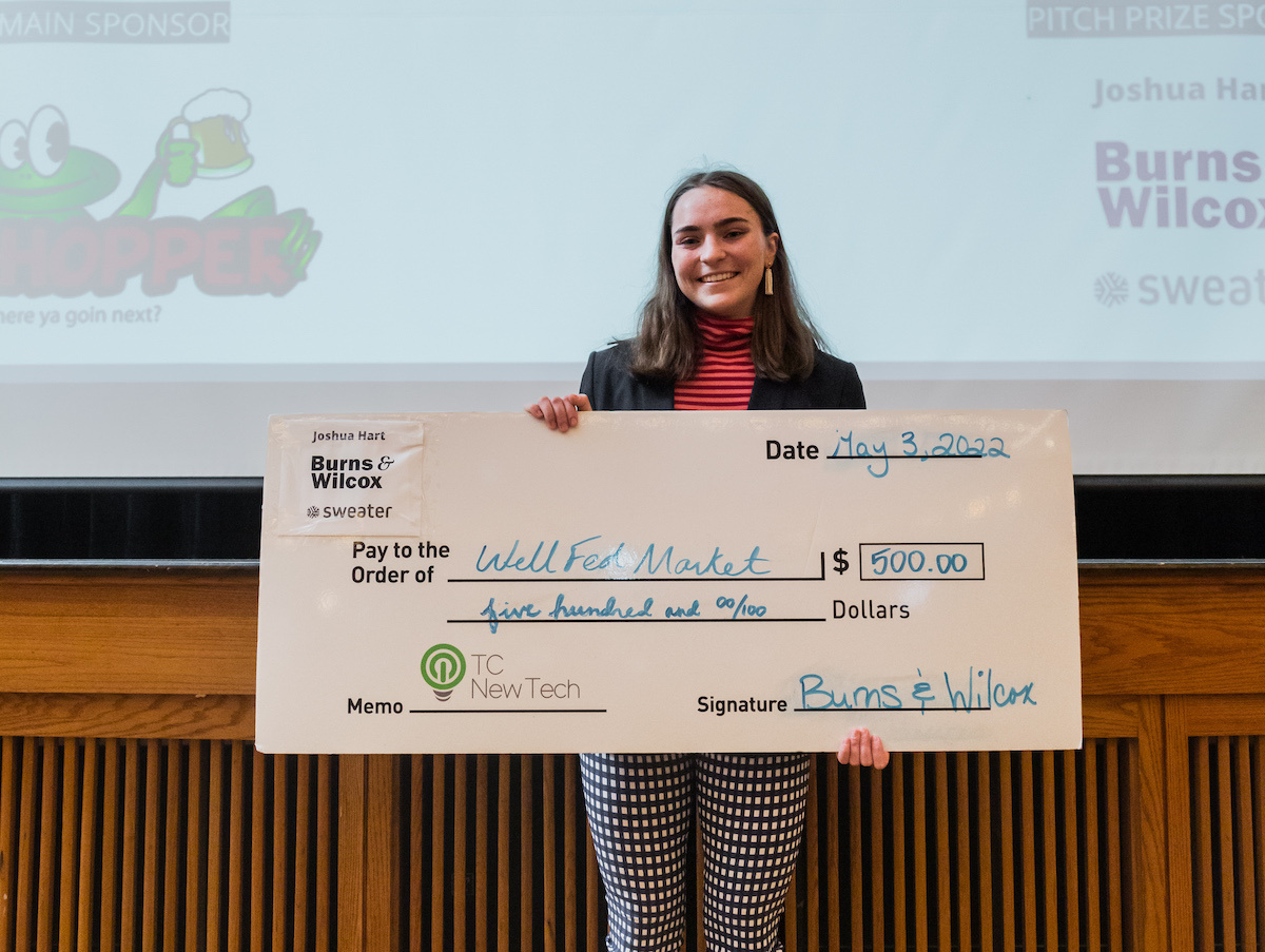 Elizabeth Saunders holding the $500 TCNewTech funding check for Wellfed Market on stage